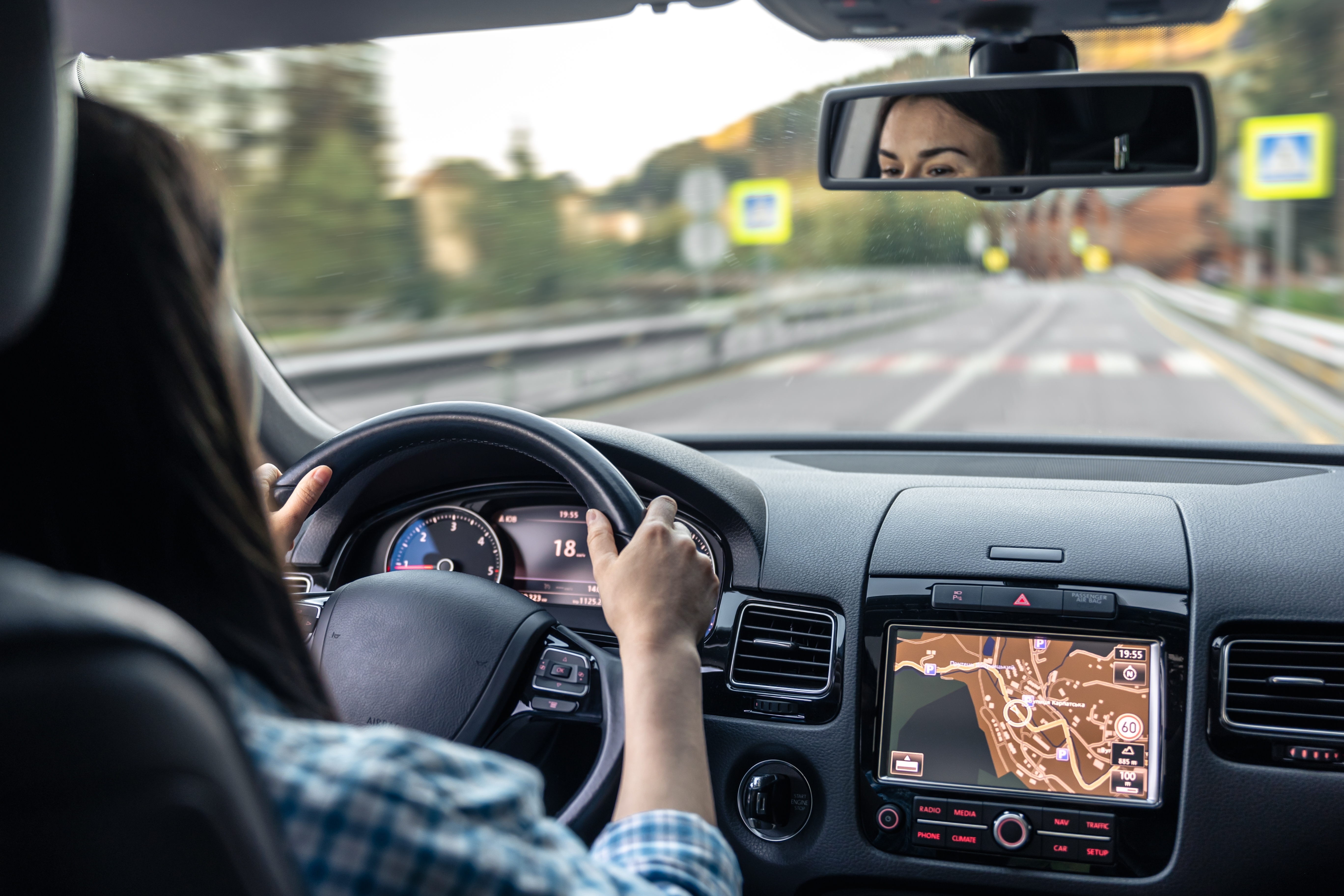 Imagem mostra uma mulher no interior de um carro dirigindo e no detalhe um espelho retrovisor
